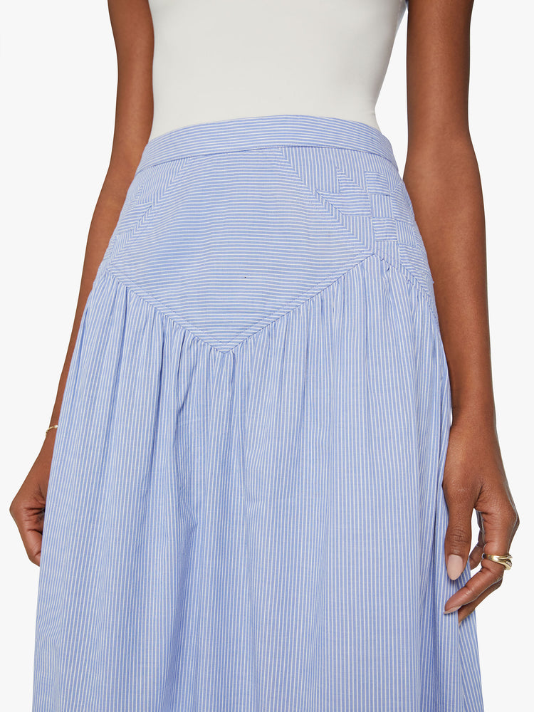 Waist view of a high waisted midi skirt with a ruffled yoke, calf-length hem and a flowy fit in a blue and white stripe pattern with a quilted snowflake motif at the hips.