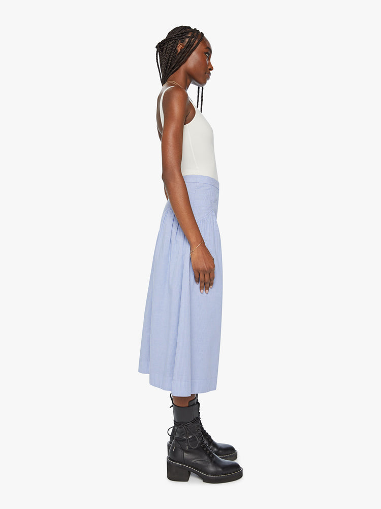 Side view of a high waisted midi skirt with a ruffled yoke, calf-length hem and a flowy fit in a blue and white stripe pattern with a quilted snowflake motif at the hips.