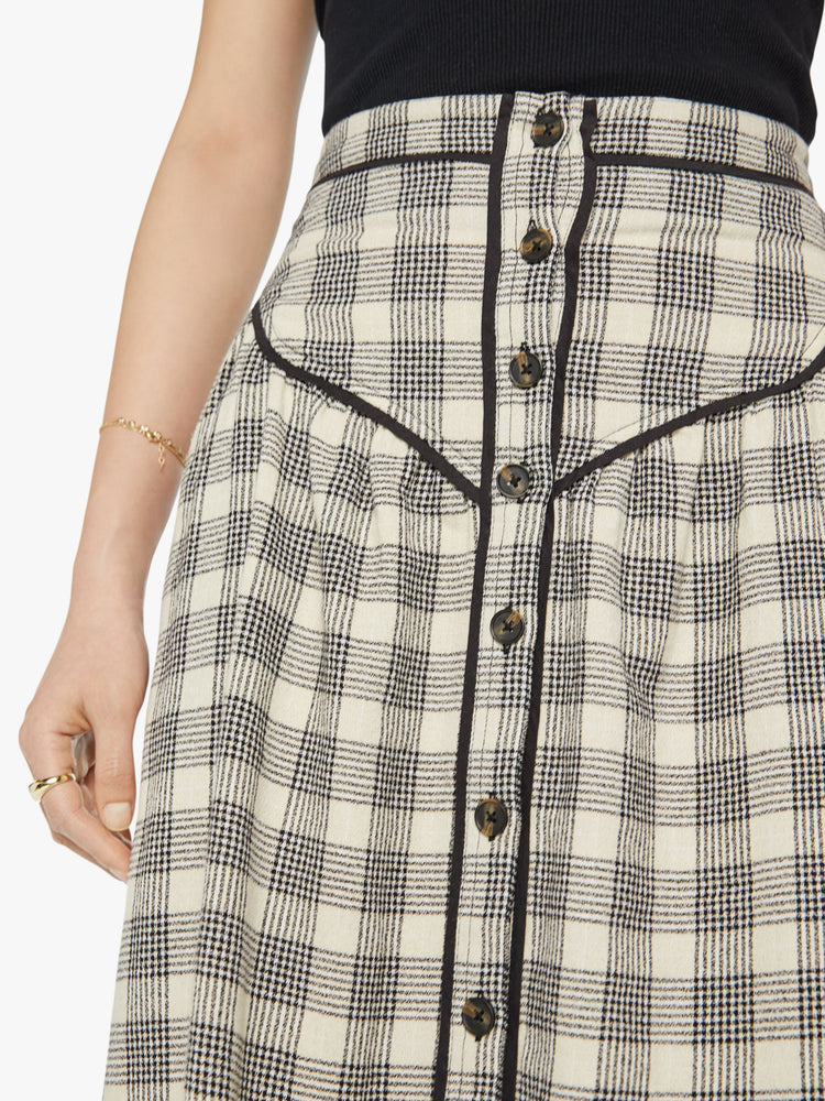 Close up view of a woman midi skirt with a high rise, buttons down the front, Western-inspired detailing at the waist and a curved hem in a black and white plaid print.