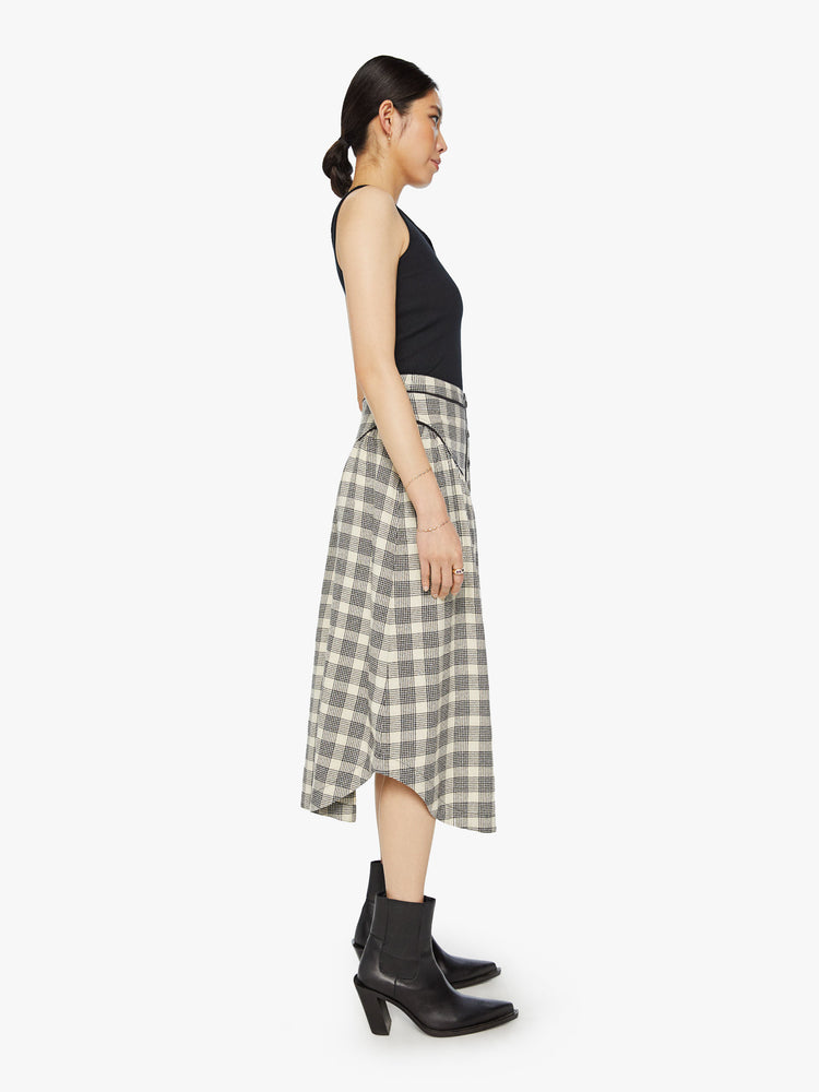 Side view of a woman midi skirt with a high rise, buttons down the front, Western-inspired detailing at the waist and a curved hem in a black and white plaid print.