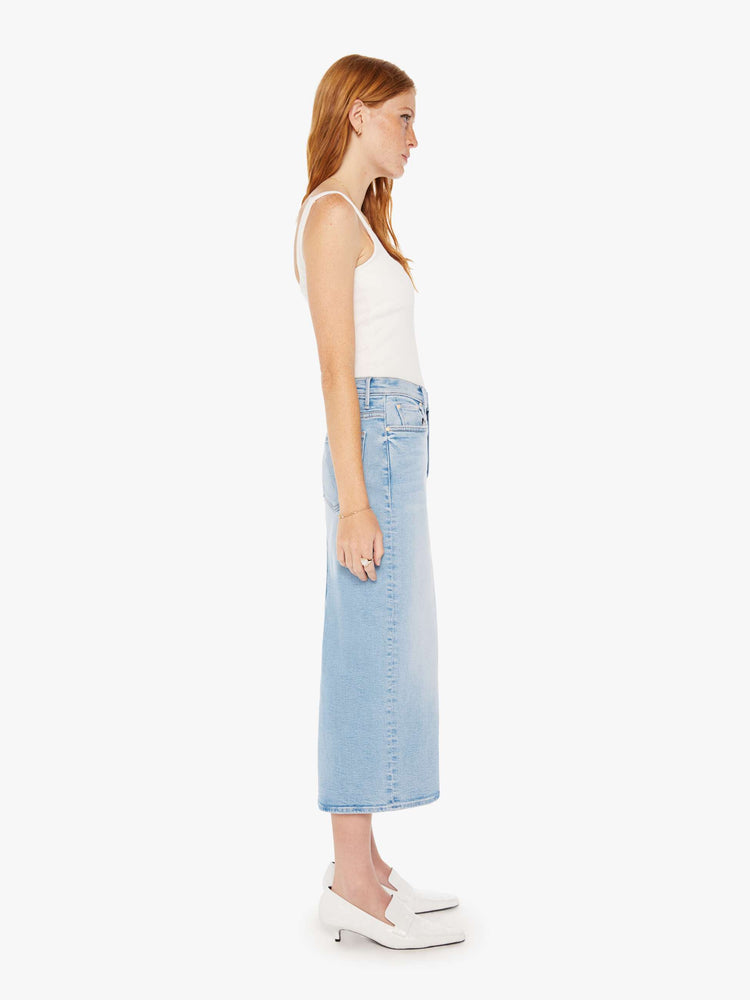 Side view of a woman light blue denim pencil skirt with a high rise, narrow fit and a thigh-high back slit.