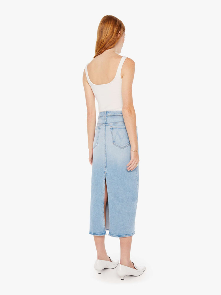 Back view of a woman light blue denim pencil skirt with a high rise, narrow fit and a thigh-high back slit.