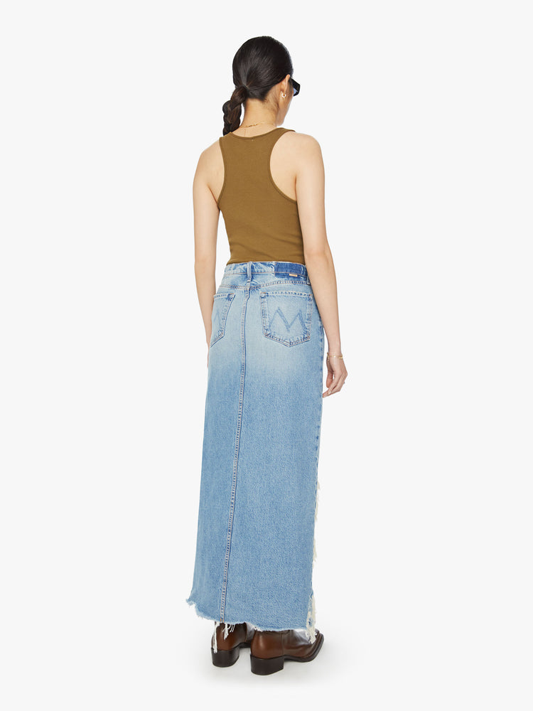 Back view of a woman denim maxi skirt with a super-high front slit, dramatically frayed hems and a relaxed fit in a light blue wash.