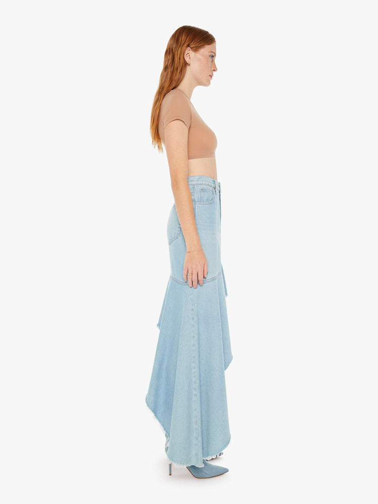 Side full body view of a woman wearing a light blue wash skirt featuring a super high rise and and exaggerated asymmetrical ruffle hem.