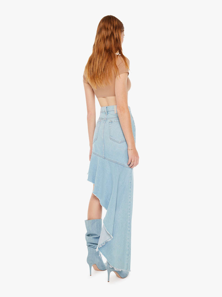 Back full body view of a woman wearing a light blue wash skirt featuring a super high rise and and exaggerated asymmetrical ruffle hem.