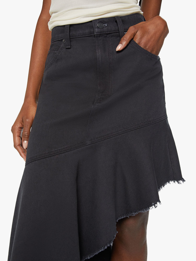 Waist close up view of a woman high-rise skirt with an angled seam at the thigh and an asymmetrical ruffle that hits at the ankle with a frayed hem in a faded black.