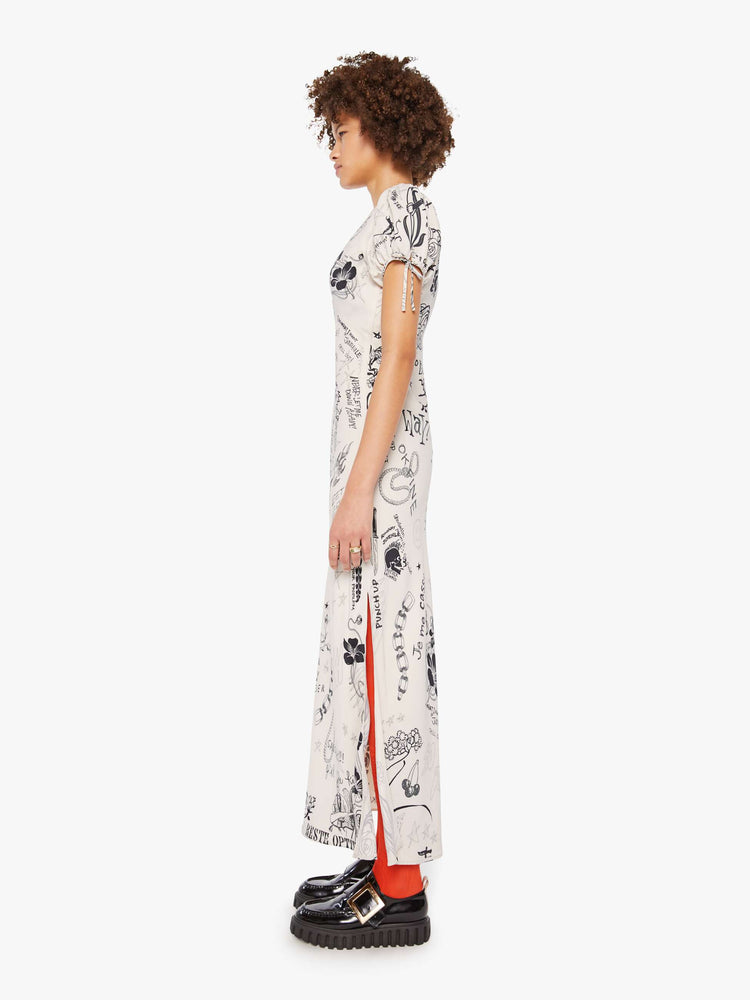 Side view of a woman in an offwhite with doodles through out slip dress with a V-neck, short puffed sleeves that tie and an ankle-length hem. 