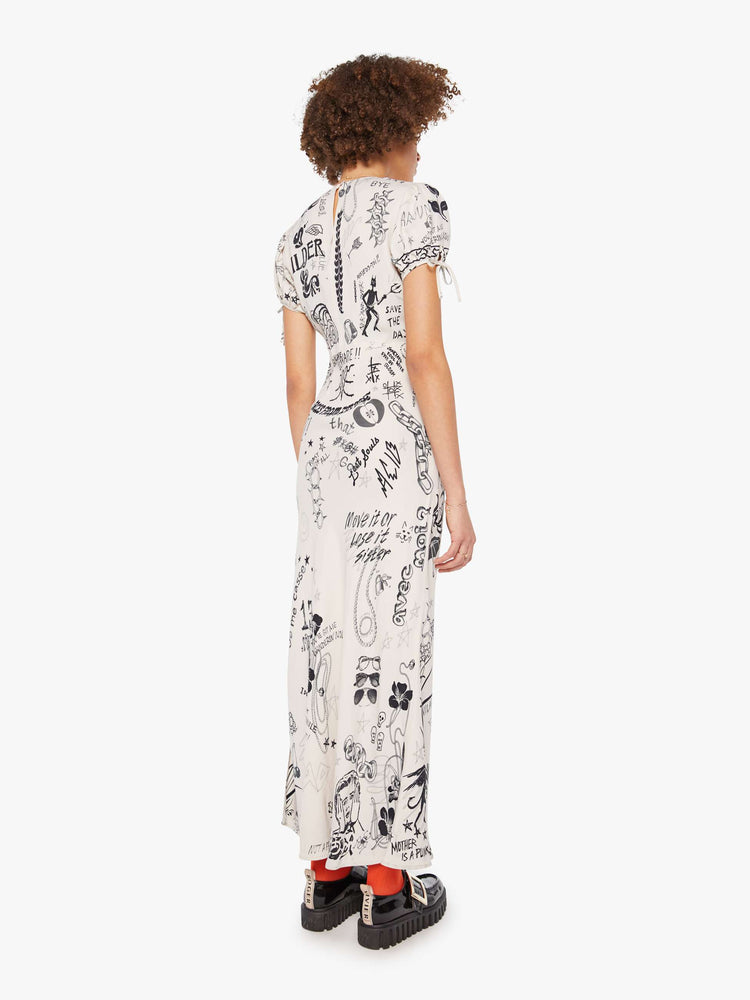 Back view of a woman in an offwhite with doodles through out slip dress with a V-neck, short puffed sleeves that tie and an ankle-length hem. 