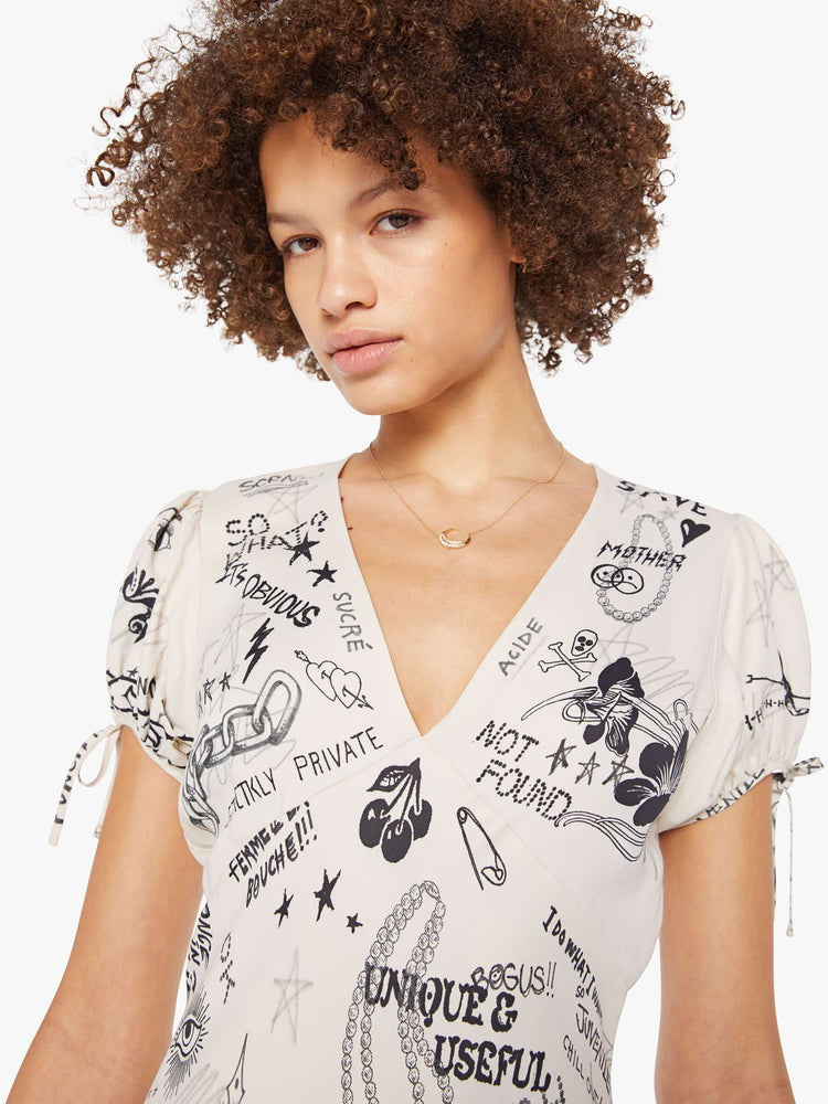 Close up view of a woman in an offwhite with doodles through out slip dress with a V-neck, short puffed sleeves that tie and an ankle-length hem. 