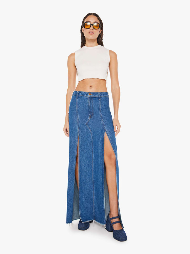 Front view of a woman mid blue wash high-rise skirt is designed with thigh-high slits up the front, a frayed hem and a flowy fit.