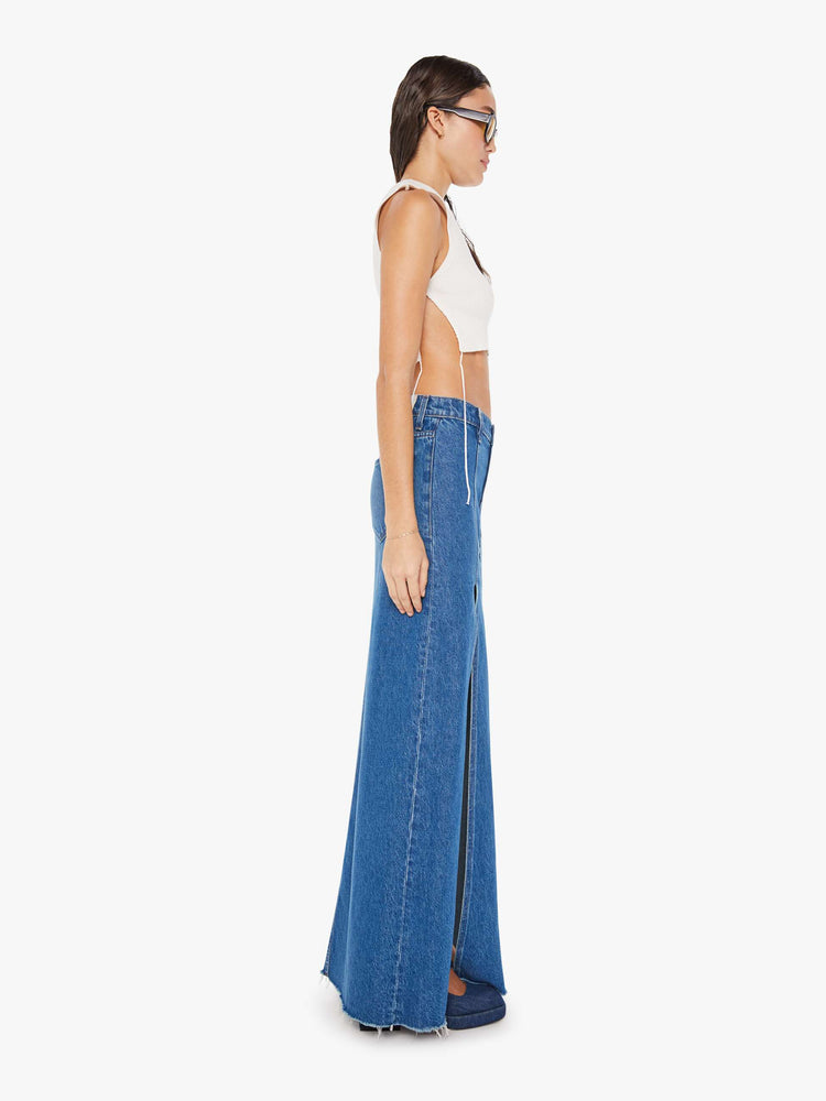 Side view of a woman mid blue wash high-rise skirt is designed with thigh-high slits up the front, a frayed hem and a flowy fit.