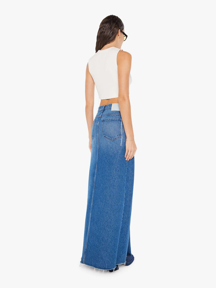 Back view of a woman mid blue wash high-rise skirt is designed with thigh-high slits up the front, a frayed hem and a flowy fit.