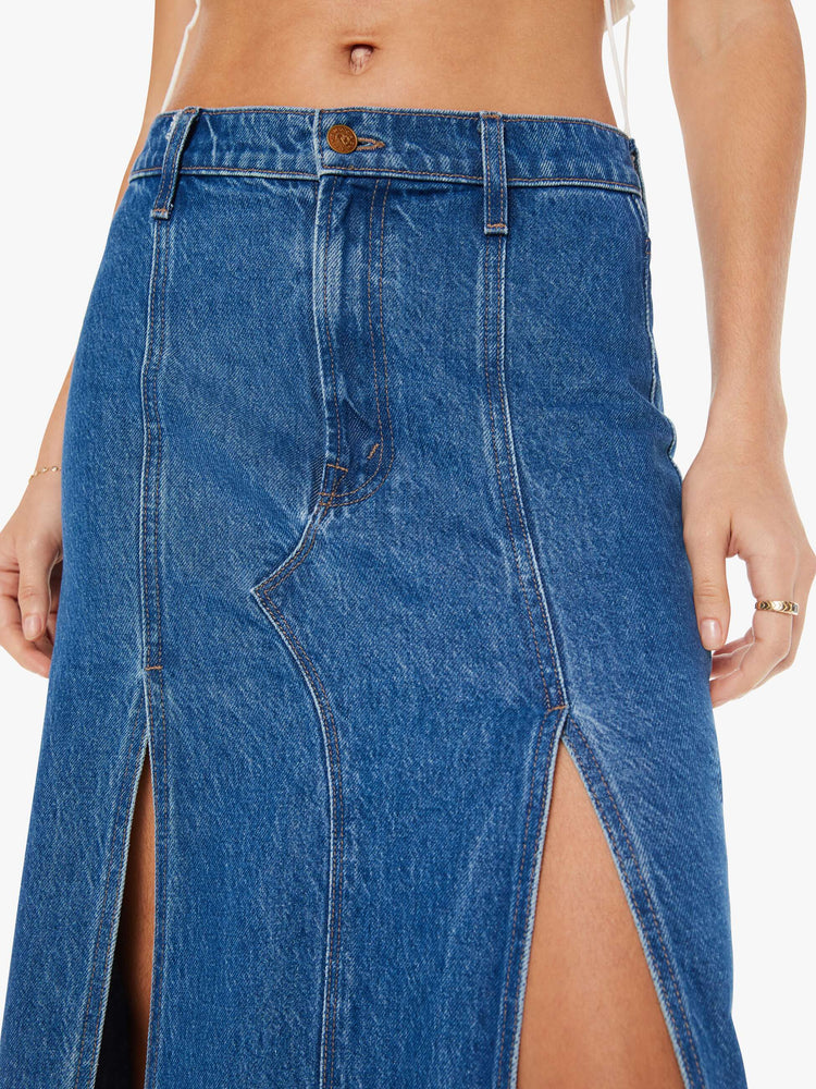 Close up view of a woman mid blue wash high-rise skirt is designed with thigh-high slits up the front, a frayed hem and a flowy fit.