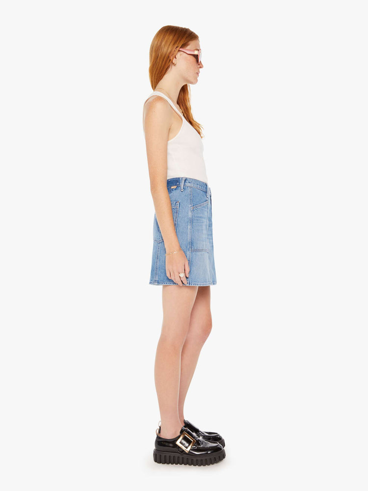 Side view of a woman denim mini skirt with a high rise, patch pockets, seams down the front and a short, thigh grazing hem in a mid blue wash.