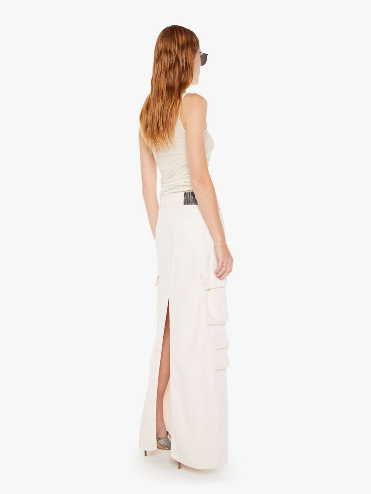 Back view of a womens off white denim skirt featuring a slouchy mid rise, cargo pockets, a back slit and a full length clean hem.