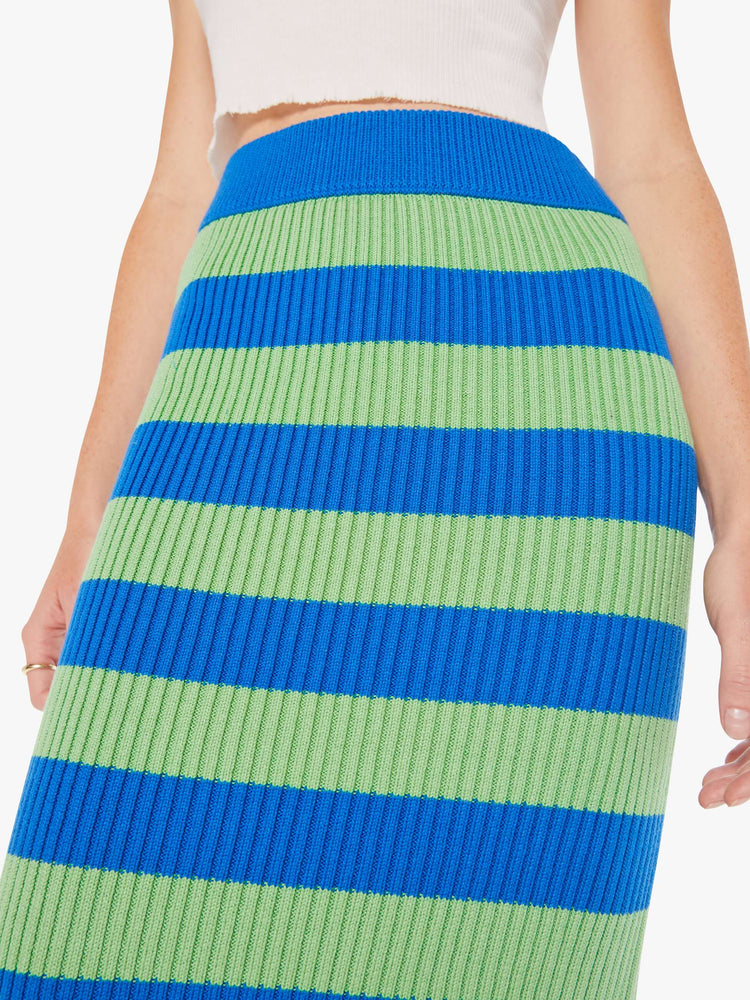 A close up detail view of a woman wearing a  green and blue striped knit skirt.