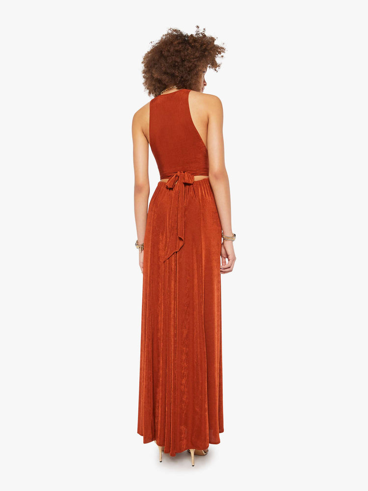 Back view of a woman in a copper V-neck maxi dress features a deep front plunge with a racerback, a tied waistband and a flowy floor-length skirt.