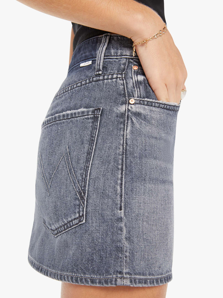 Side close up view of a womens grey denim skirt featuring a relaxed mid rise and clean hem.