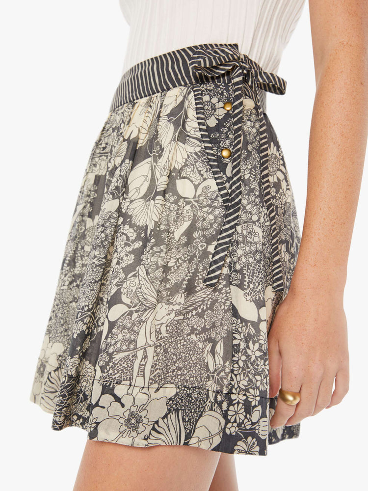 Side close up view of a womens wrap skirt featuring a black and white floral print and a contrast waist tie.