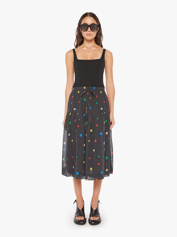 Front view of a woman in a black with colorful daisy print  lightweight midi skirt with an elastic drawstring waistband and a ruffled tier for a loose, flowy fit.