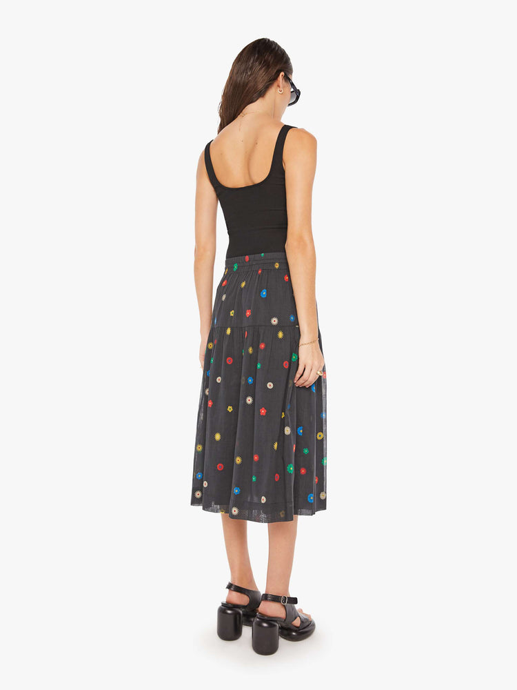 Back view of a woman in a black with colorful daisy print lightweight midi skirt with an elastic drawstring waistband and a ruffled tier for a loose, flowy fit.