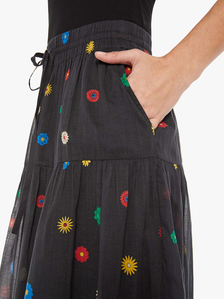 Close up view of a woman in a black with colorful daisy print lightweight midi skirt with an elastic drawstring waistband and a ruffled tier for a loose, flowy fit.