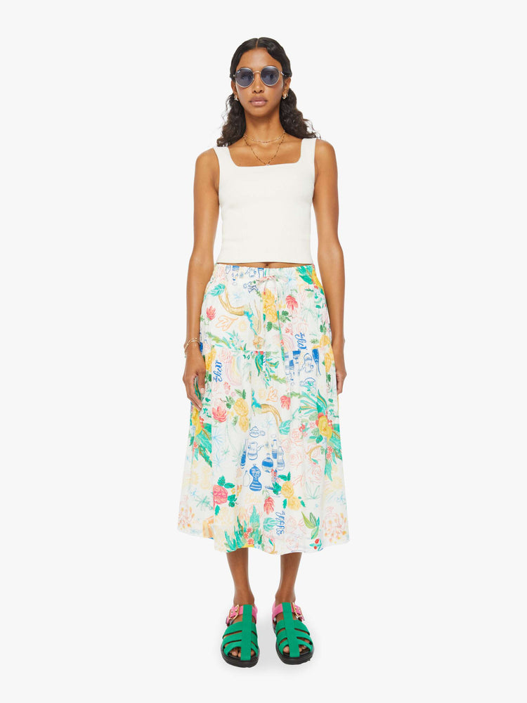 Front view of a woman in a white midi skirt with an elastic drawstring waistband and a ruffled tier with hand-drawn doodles throughout and blue stitching at the hem.