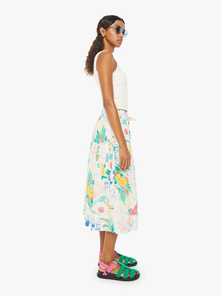Side view of a woman in a white midi skirt with an elastic drawstring waistband and a ruffled tier with hand-drawn doodles throughout and blue stitching at the hem.