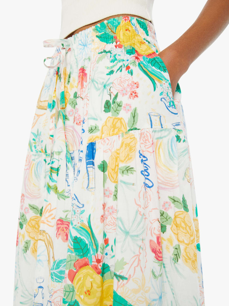 Detailed view of a woman in a white midi skirt with an elastic drawstring waistband and a ruffled tier with hand-drawn doodles throughout and blue stitching at the hem.