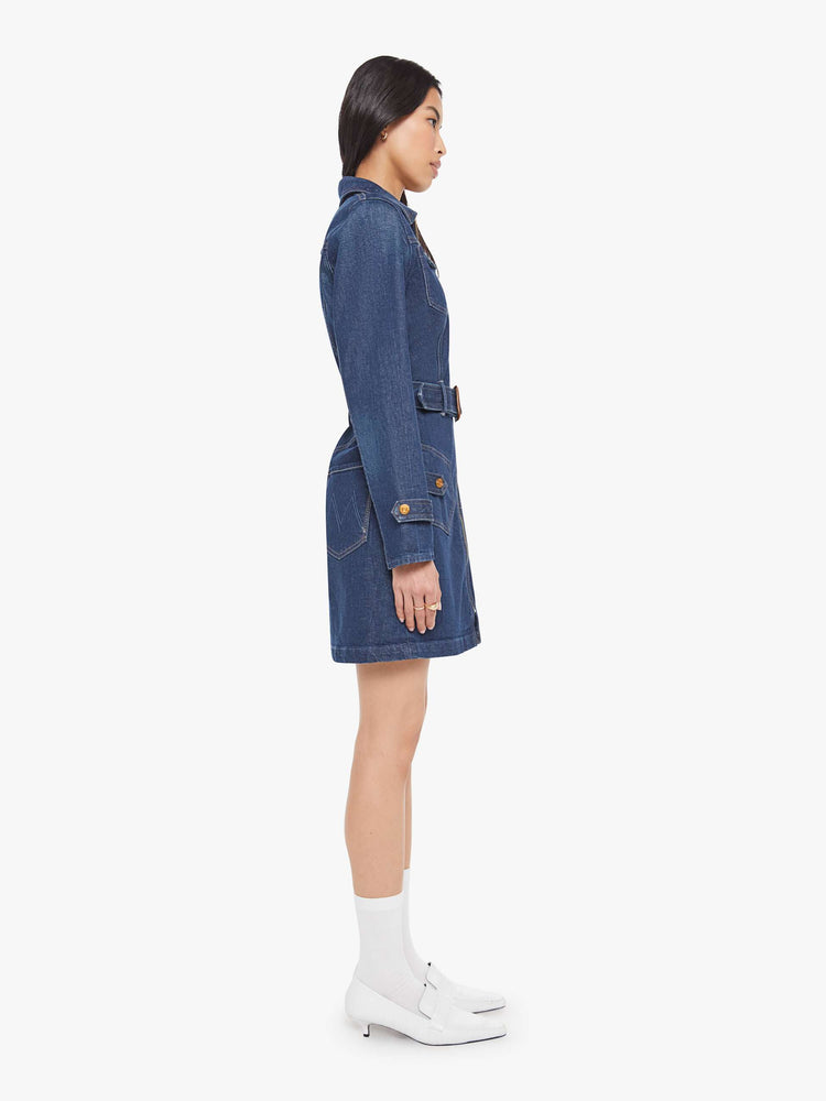 Side view of a woman in collared denim mini dress with long sleeves, a zip closure, belted waist, patch pockets and a hem that hits mid-thigh.