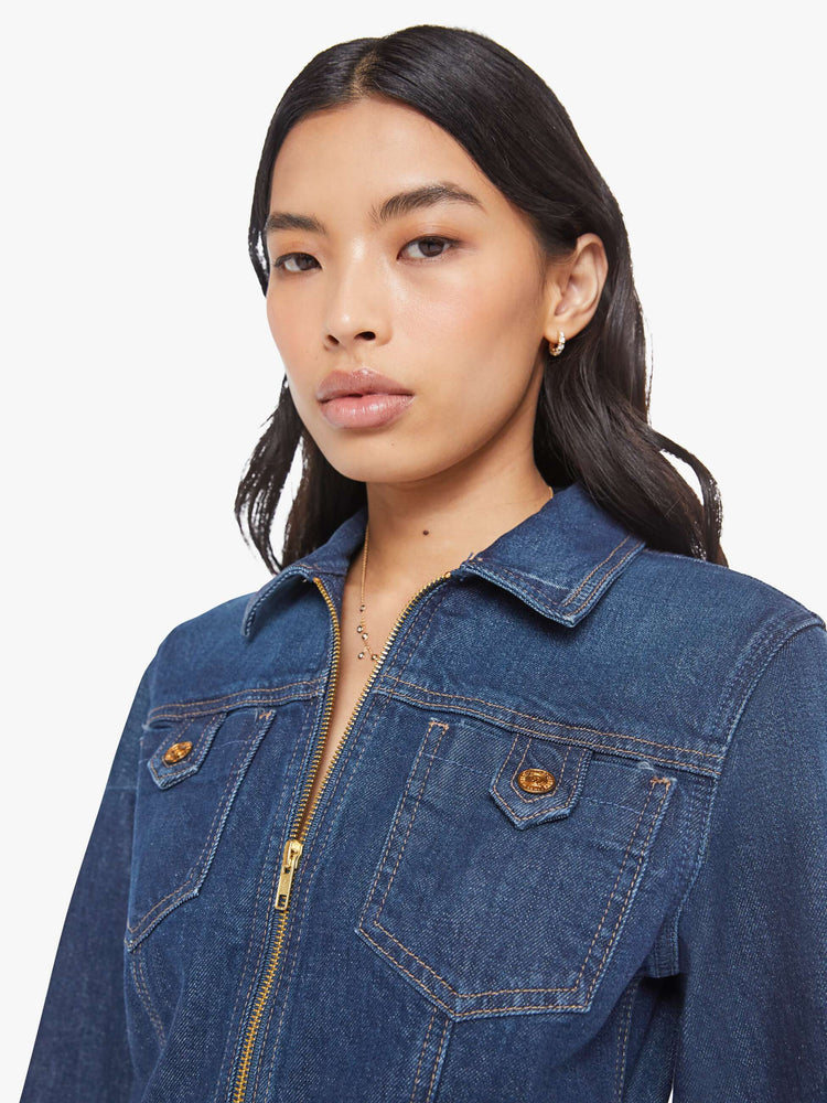 Close up view of a woman in collared denim mini dress with long sleeves, a zip closure, belted waist, patch pockets and a hem that hits mid-thigh.