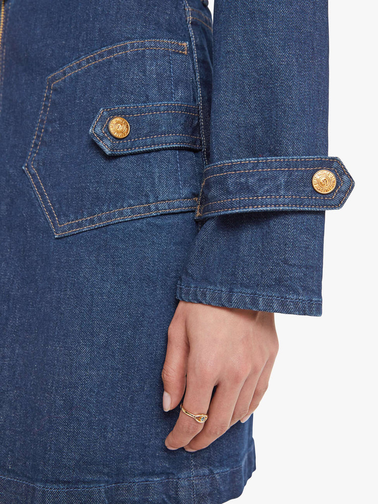 Close up view of a woman in collared denim mini dress with long sleeves, a zip closure, belted waist, patch pockets and a hem that hits mid-thigh.