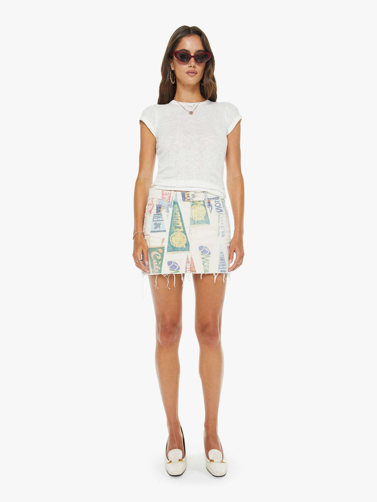 Full body view of a woman in an off-white with a faded pennant print throughout low-slung mini skirt with a zip fly and a raw, frayed hem.