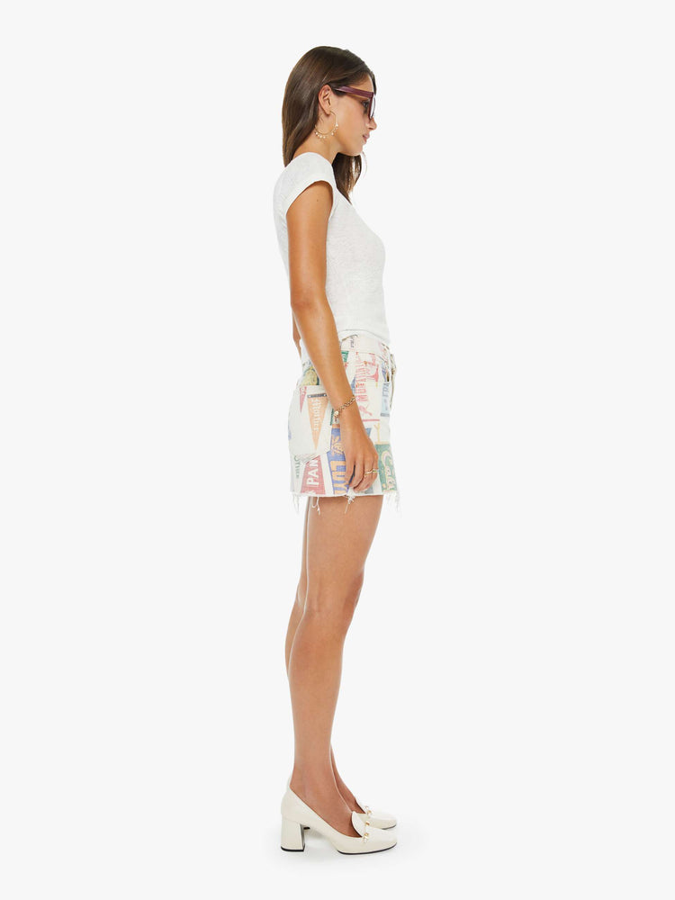 Side view of a woman in an off-white with a faded pennant print throughout low-slung mini skirt with a zip fly and a raw, frayed hem.