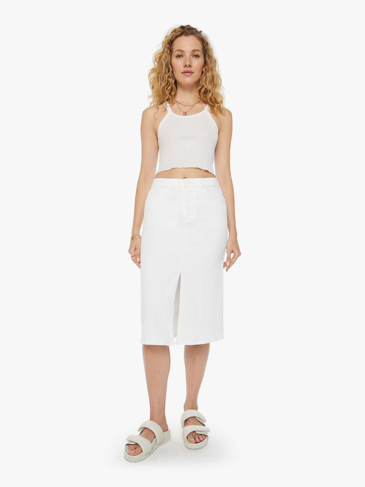Front view of a woman in a white midi skirt with a button fly, slim fit and thigh-high front slit paired with a white tank top.