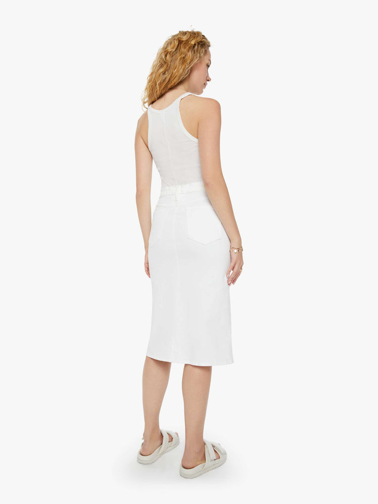 Back view of a woman in a white midi skirt with a button fly, slim fit and thigh-high front slit paired with a white tank top.