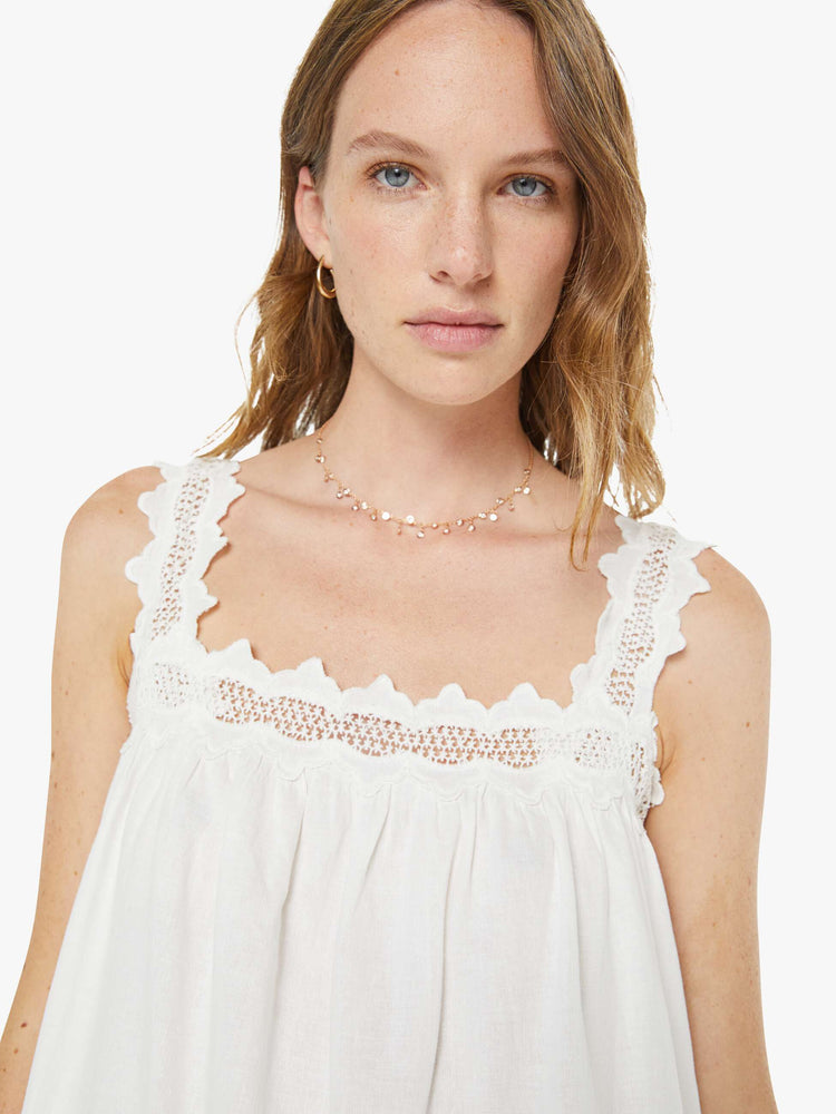 Close up view of a woman in a white embroidery vintage-inspired maxi dress with a square neck, thick embroidered straps and a loose, flowy fit. 