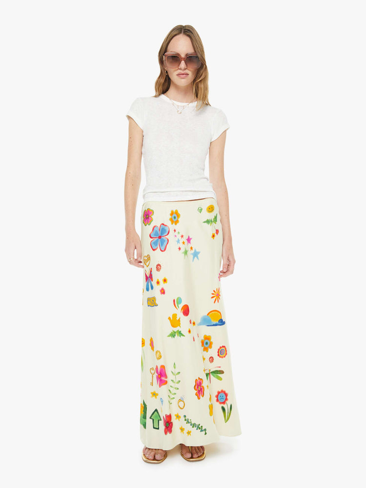 Front view of a woman in maxi slip skirt with a mid rise, loose fit and an ankle-length hem in offwhite with colorful flowers, stars, butterflies, leaves and more throughout.