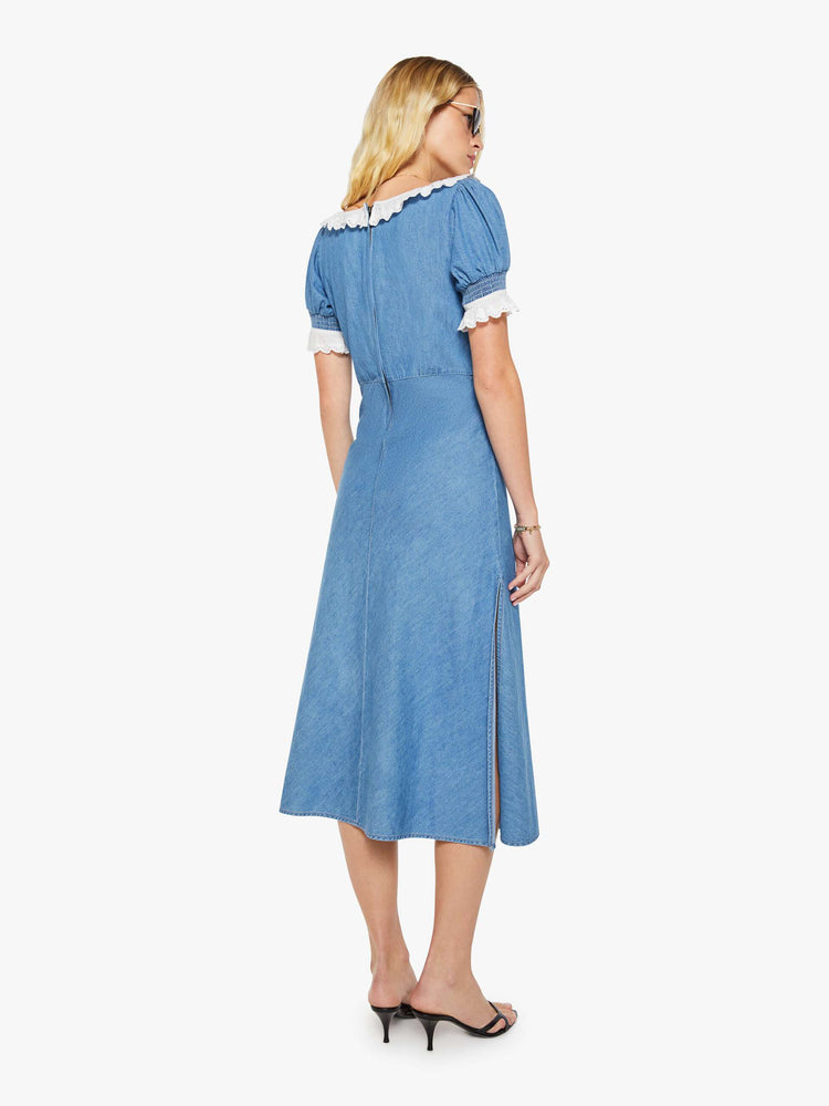 Back view of a woman in a denim maxi dress with a scoop neck, short balloon sleeves, a gathered bodice, thigh-high side slit and a calf-length hem.