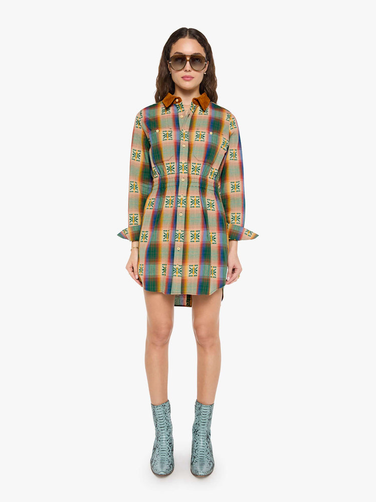 Front view of a woman in a vintage inspired plaid button-up mini dress with long sleeves, an elastic waistband, patch pockets and a curved hem.