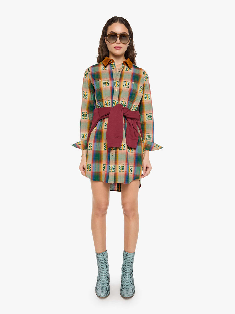 Front view of a woman in a vintage inspired plaid button-up mini dress with long sleeves, an elastic waistband, patch pockets and a curved hem.