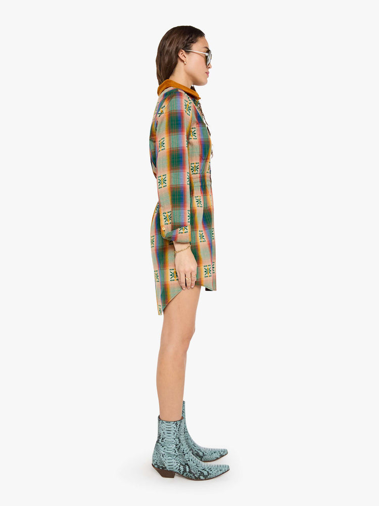 Side view of a woman in a vintage inspired plaid button-up mini dress with long sleeves, an elastic waistband, patch pockets and a curved hem.