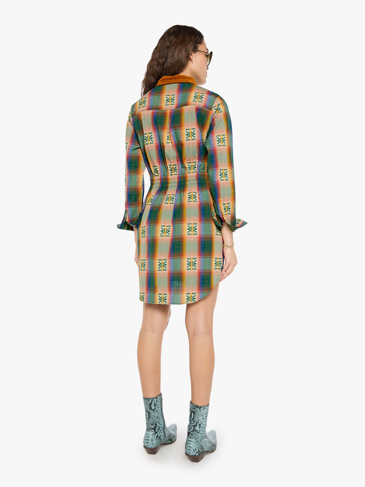 Back view of a woman in a vintage inspired plaid button-up mini dress with long sleeves, an elastic waistband, patch pockets and a curved hem.