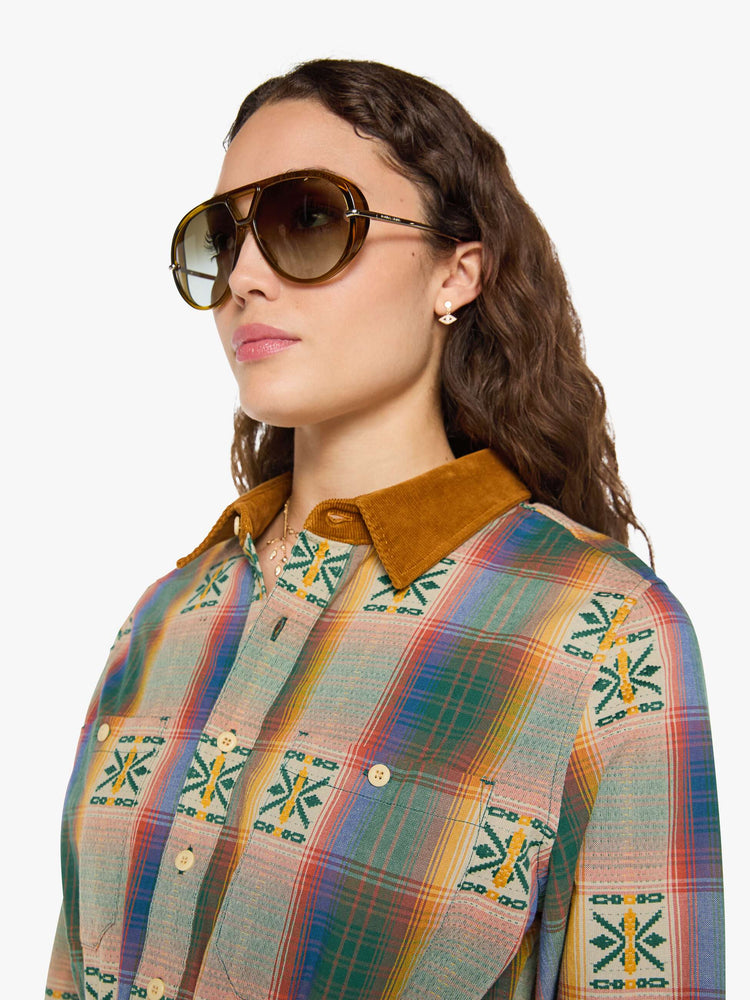 Close up view of a woman in a vintage inspired plaid button-up mini dress with long sleeves, an elastic waistband, patch pockets and a curved hem.