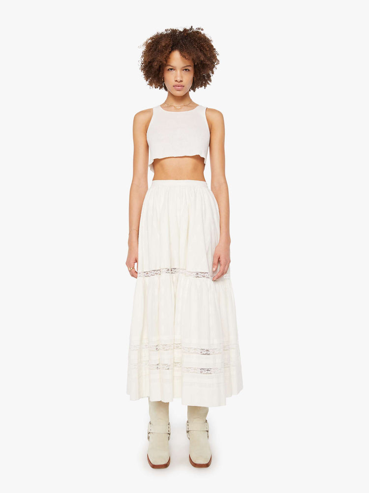 Front view of a woman in a white flowy maxi skirt with a high rise, elastic waist and a calf-length hem.