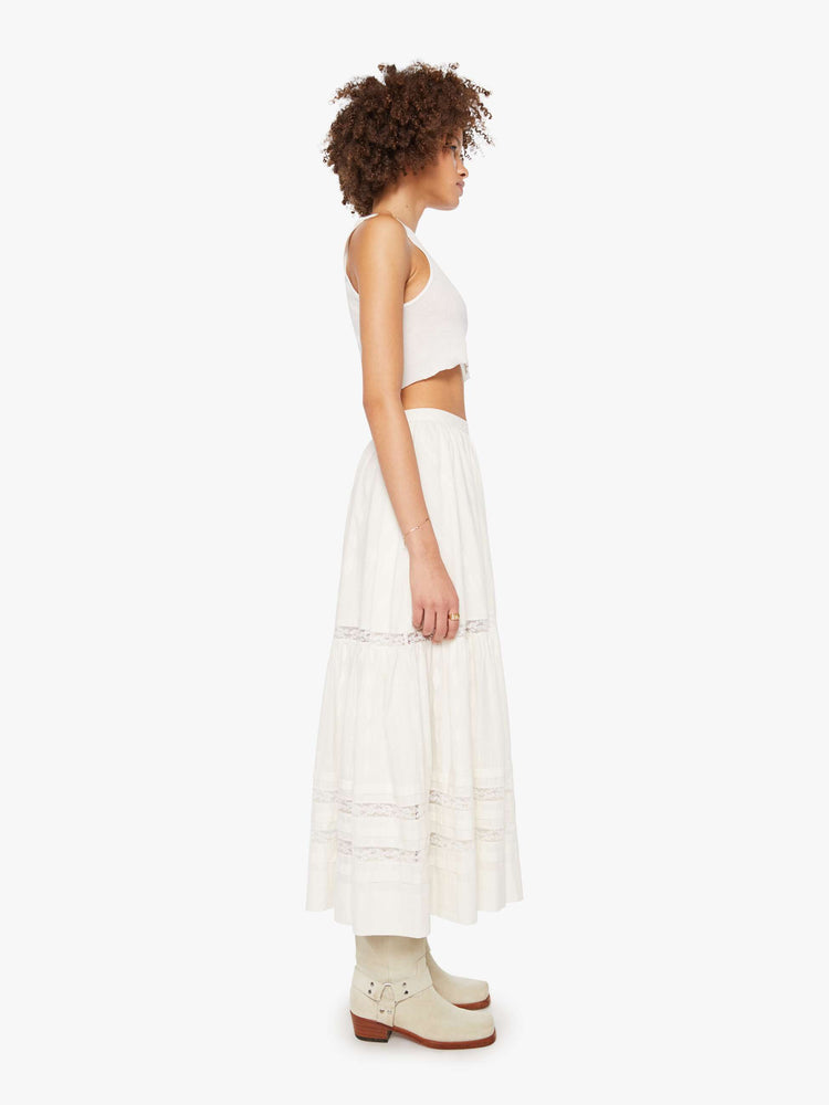 Side view of a woman in a white flowy maxi skirt with a high rise, elastic waist and a calf-length hem.
