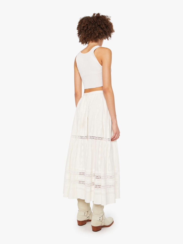 Back view of a woman in a white flowy maxi skirt with a high rise, elastic waist and a calf-length hem.