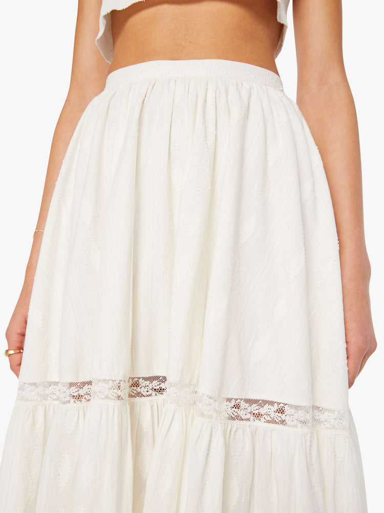 Close up view of a woman in a white flowy maxi skirt with a high rise, elastic waist and a calf-length hem.