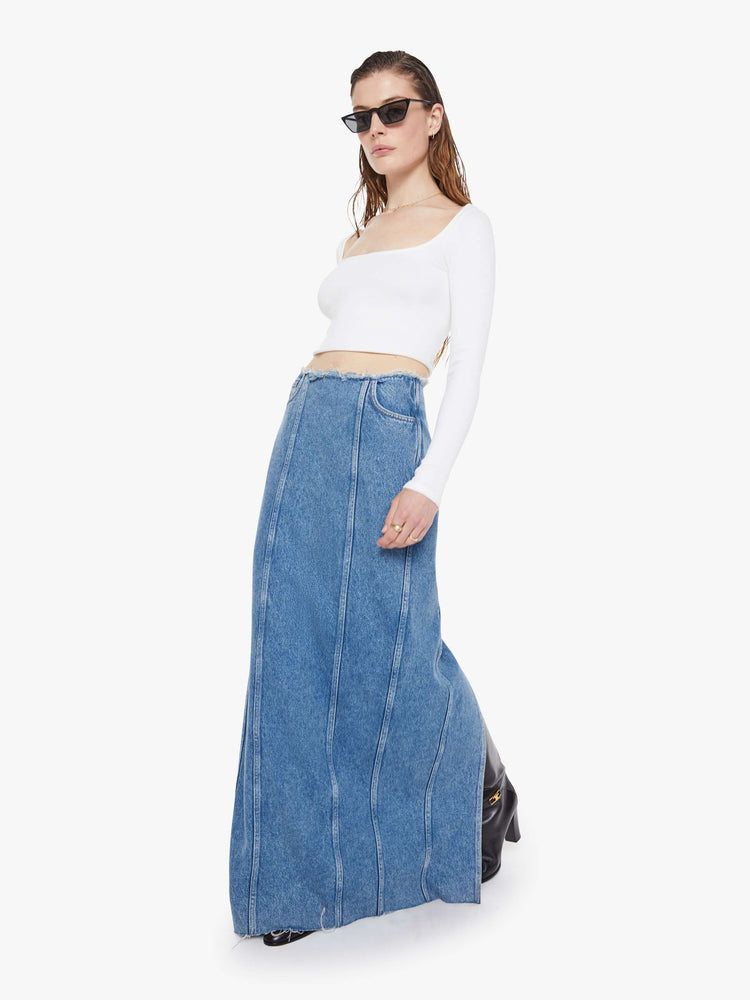 Walking view of a med blue high-waisted skirt is designed with a frayed waistband and hem, back-zip closure, pintuck details down the front and a loose fit.