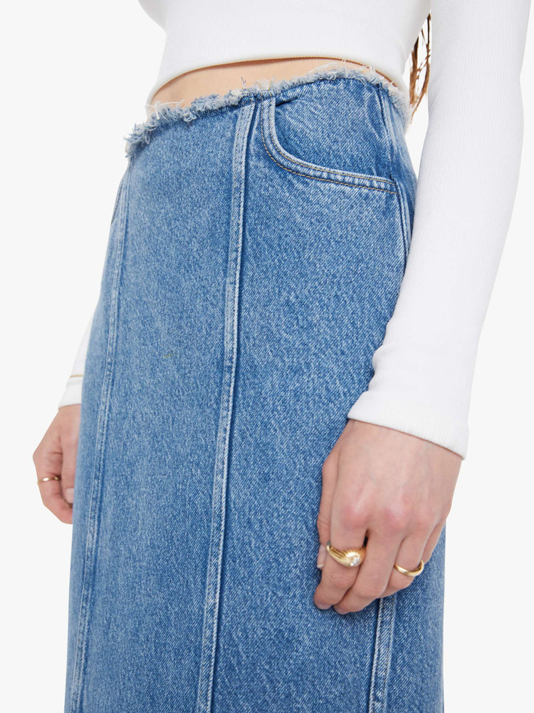 Close up view of a med blue high-waisted skirt is designed with a frayed waistband and hem, back-zip closure, pintuck details down the front and a loose fit.